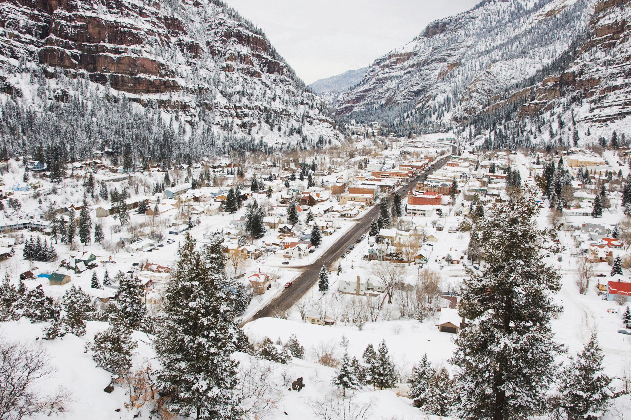 Snow-covered mountain valley town surrounded by towering cliffs, evergreen trees and winter landscapes.