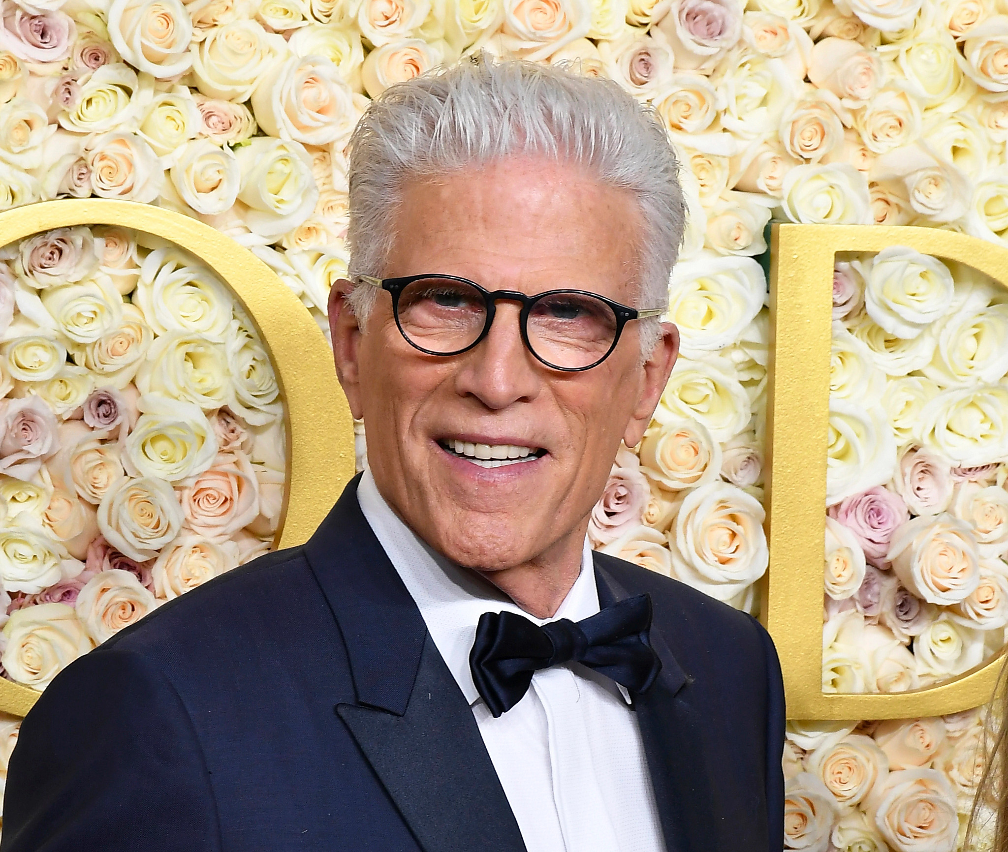 ted danson posing in front of a wall of flowers