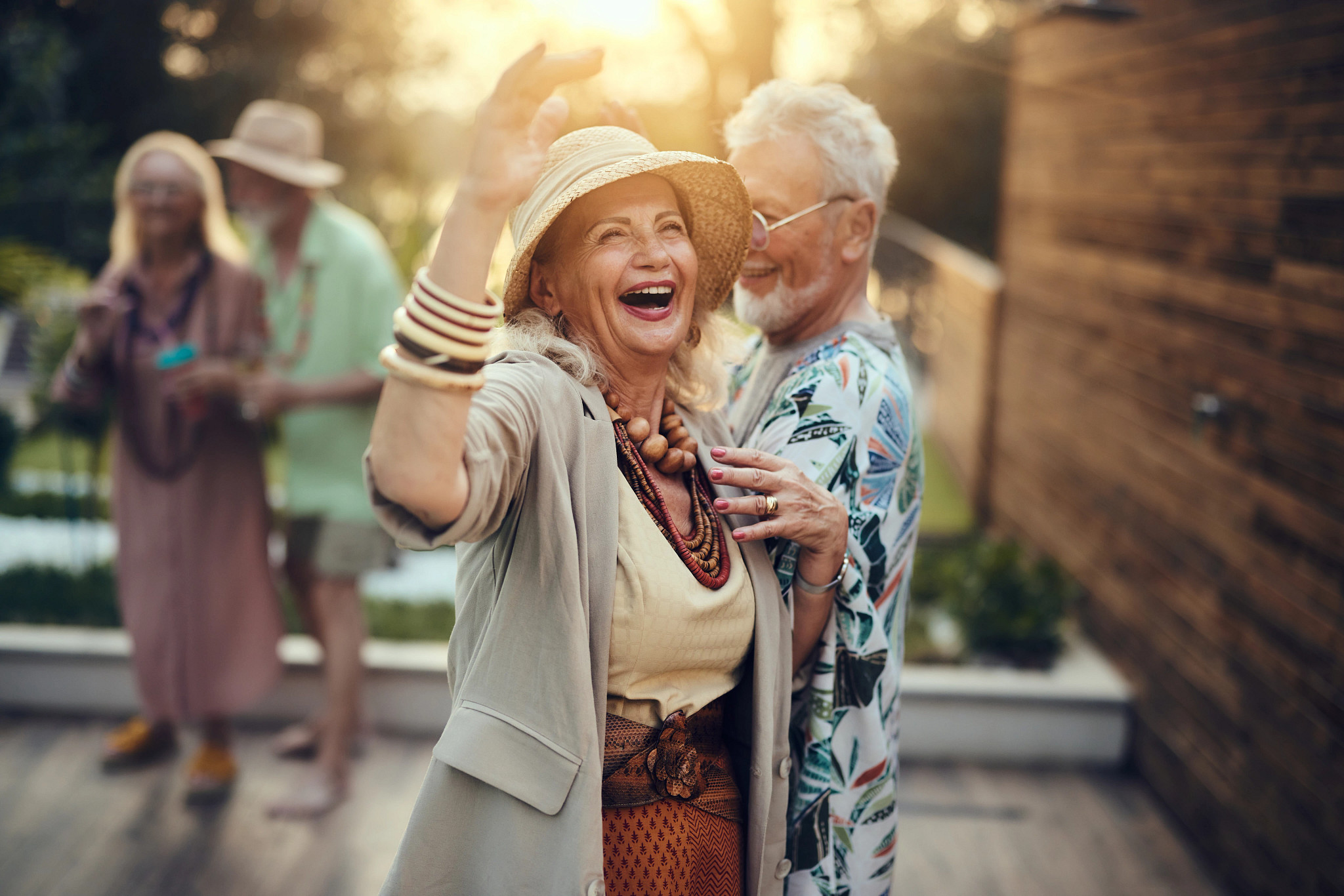 Carefree senior couple having fun while dancing during a party in the backyard at sunset. Focus is on woman.