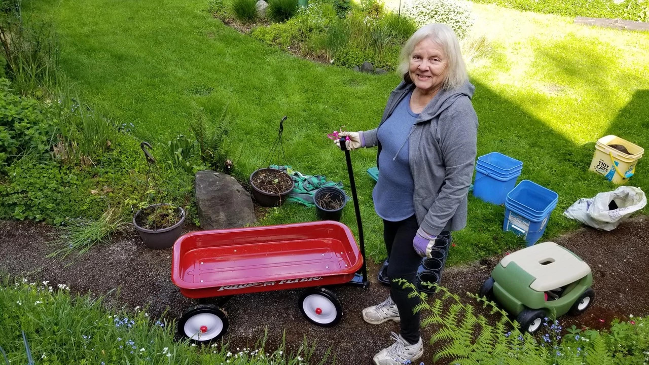 a woman stands next to a red wagon in a garden