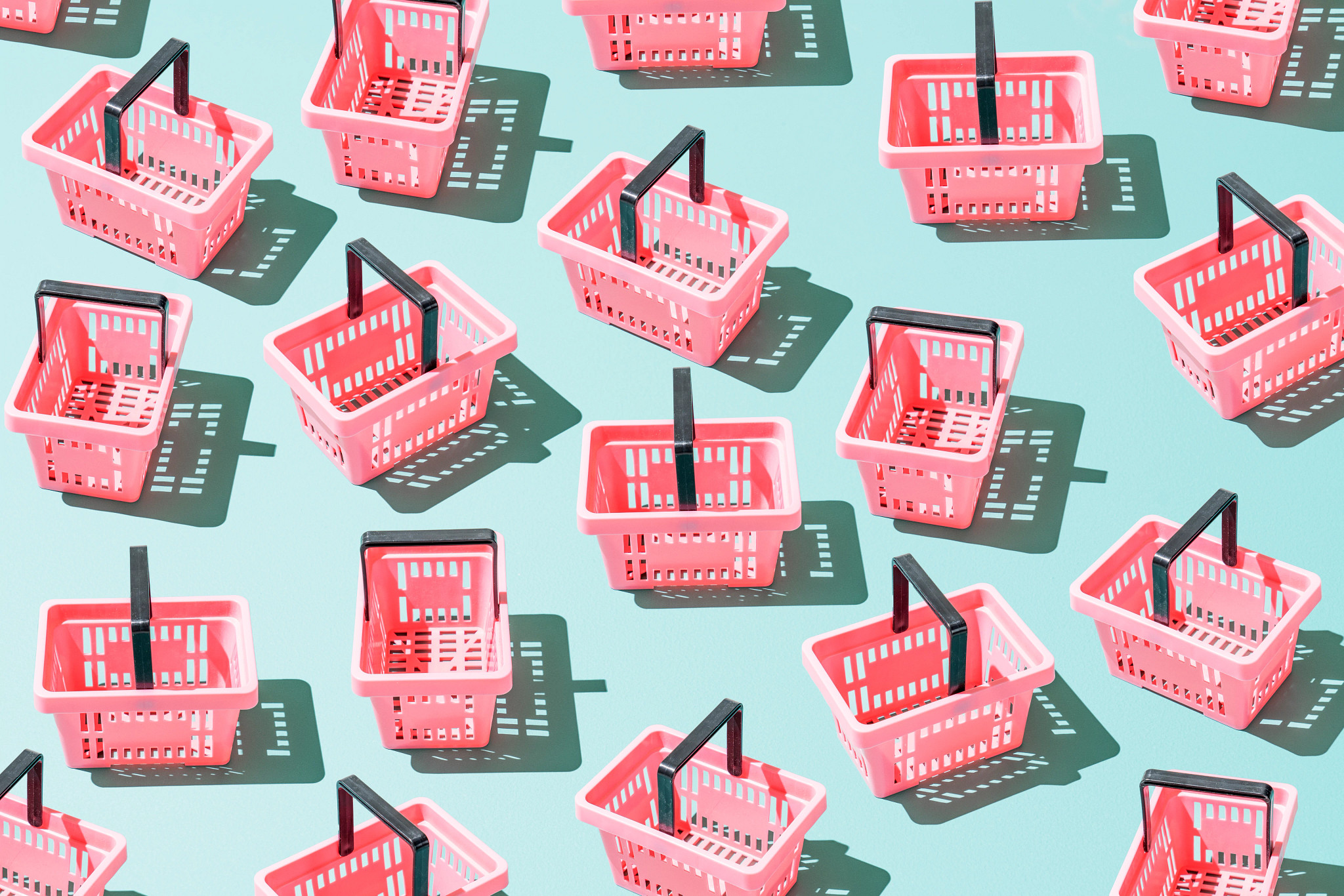 A photo illustration shows a ¾ view of numerous empty handheld grocery baskets castings shadows on a foam green surface.