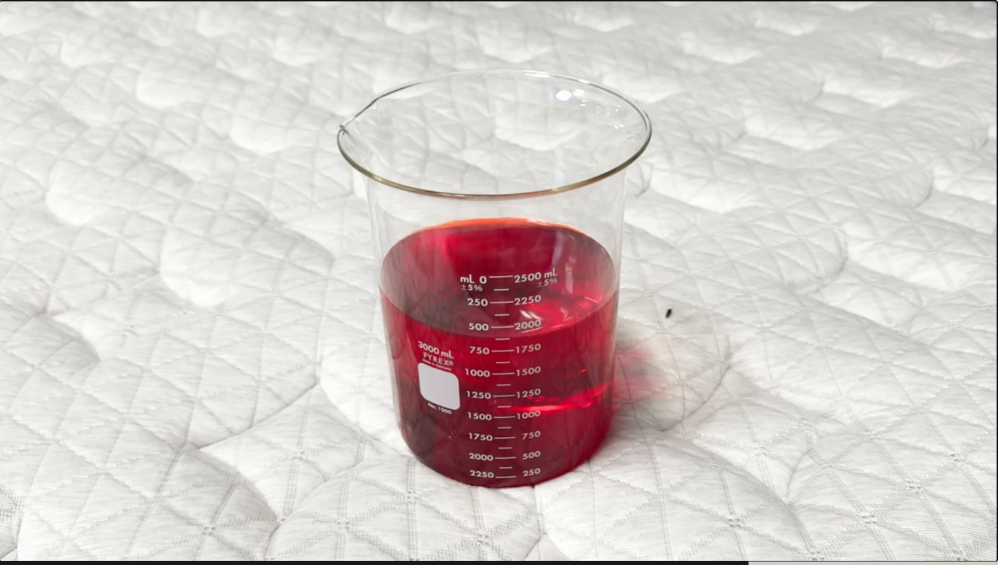 A beaker of red liquid rests on top of a mattress