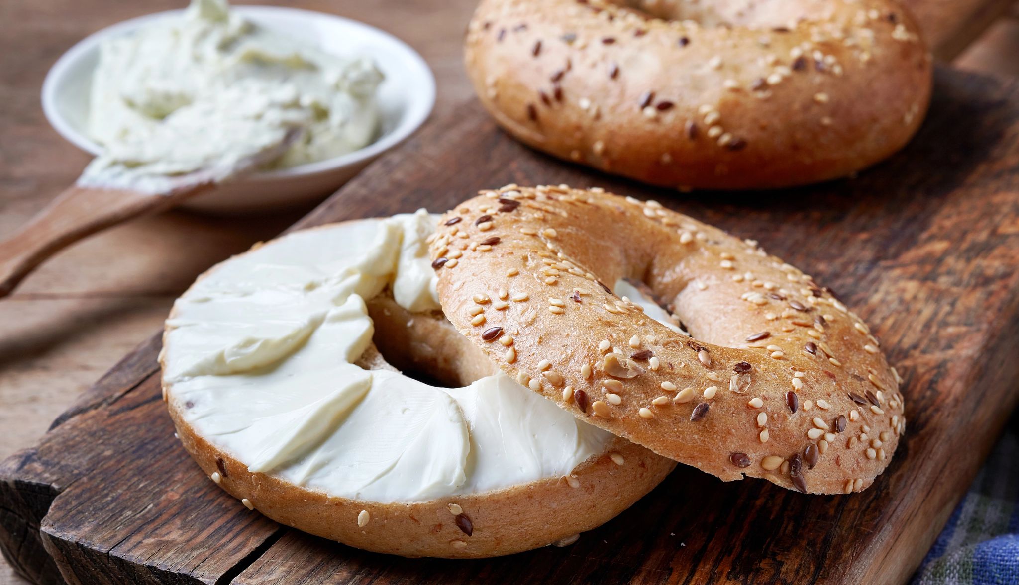 a bagel topped with cream cheese on a wooden serving tray