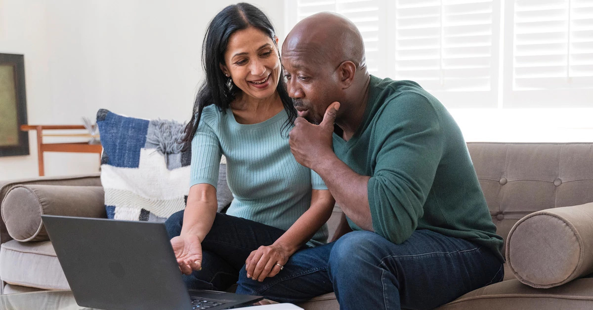 Woman (L) and man (R) sitting on couch looking at laptop