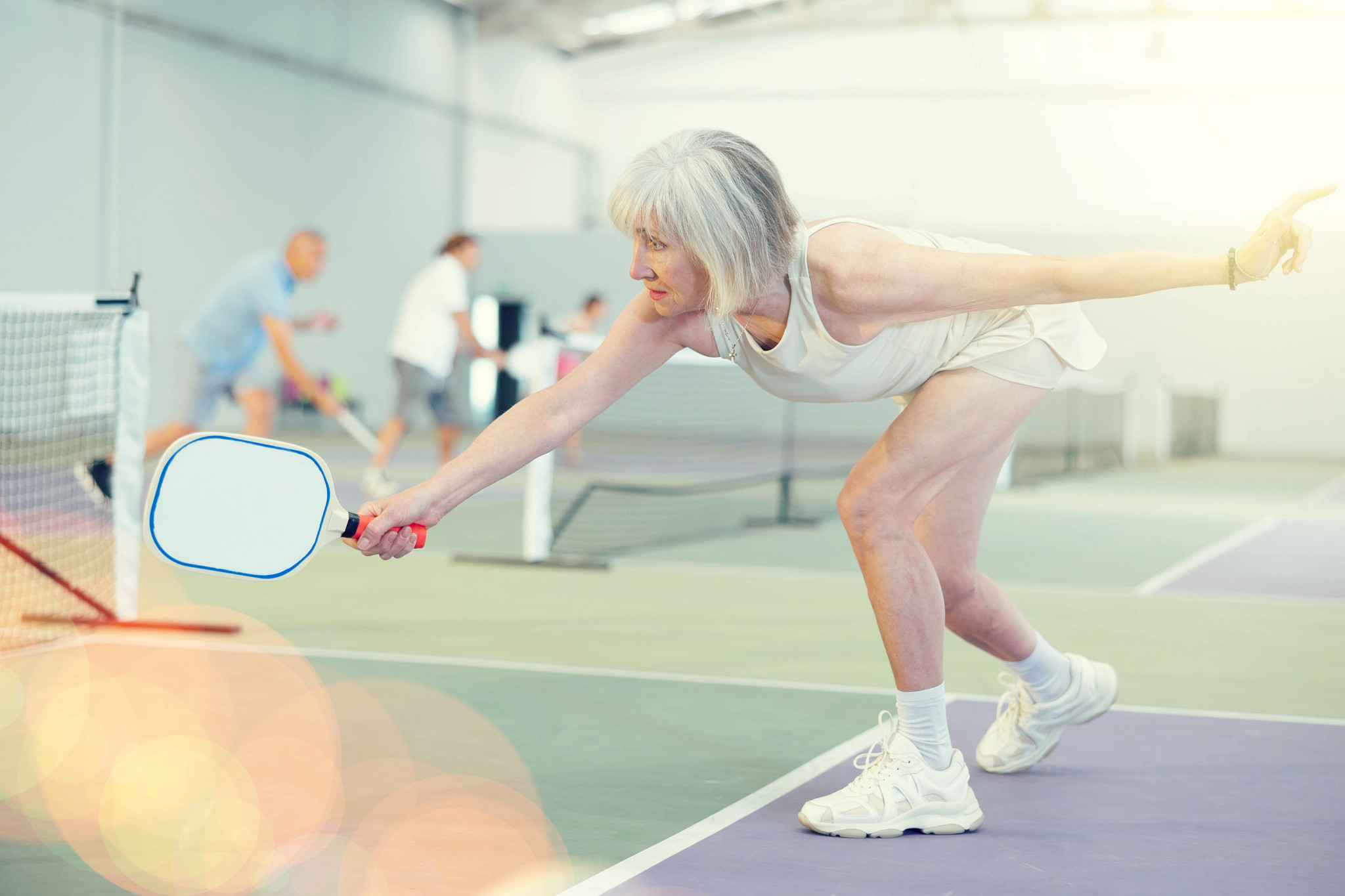 A woman and a man are practicing pickleball in an indoor court - others are in the background practicing as well