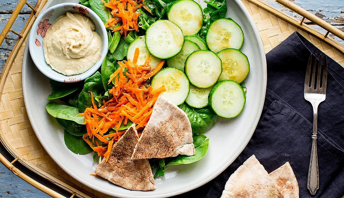 A close-up view of a green salad with pita bread and hummus on a plate