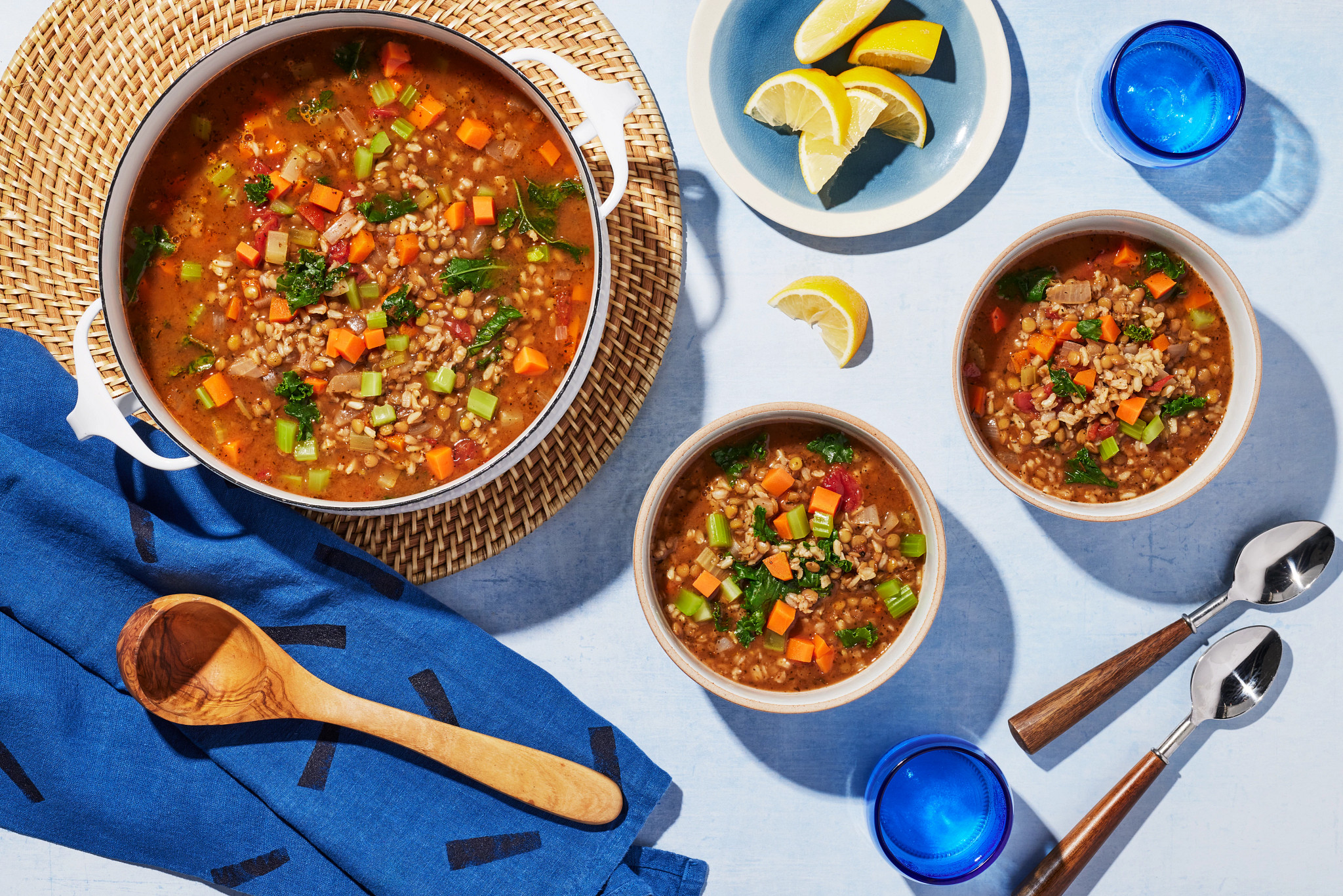 Hearty plant-based lentil soup with carrots, celery, and greens served in a pot and bowls with lemon wedges