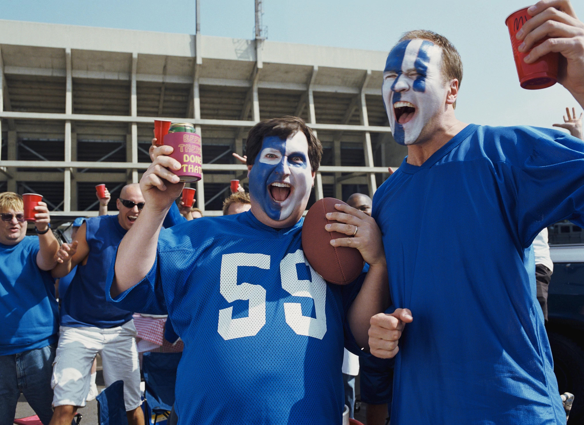 Men with painted faces holding red cup in stadium parking lot