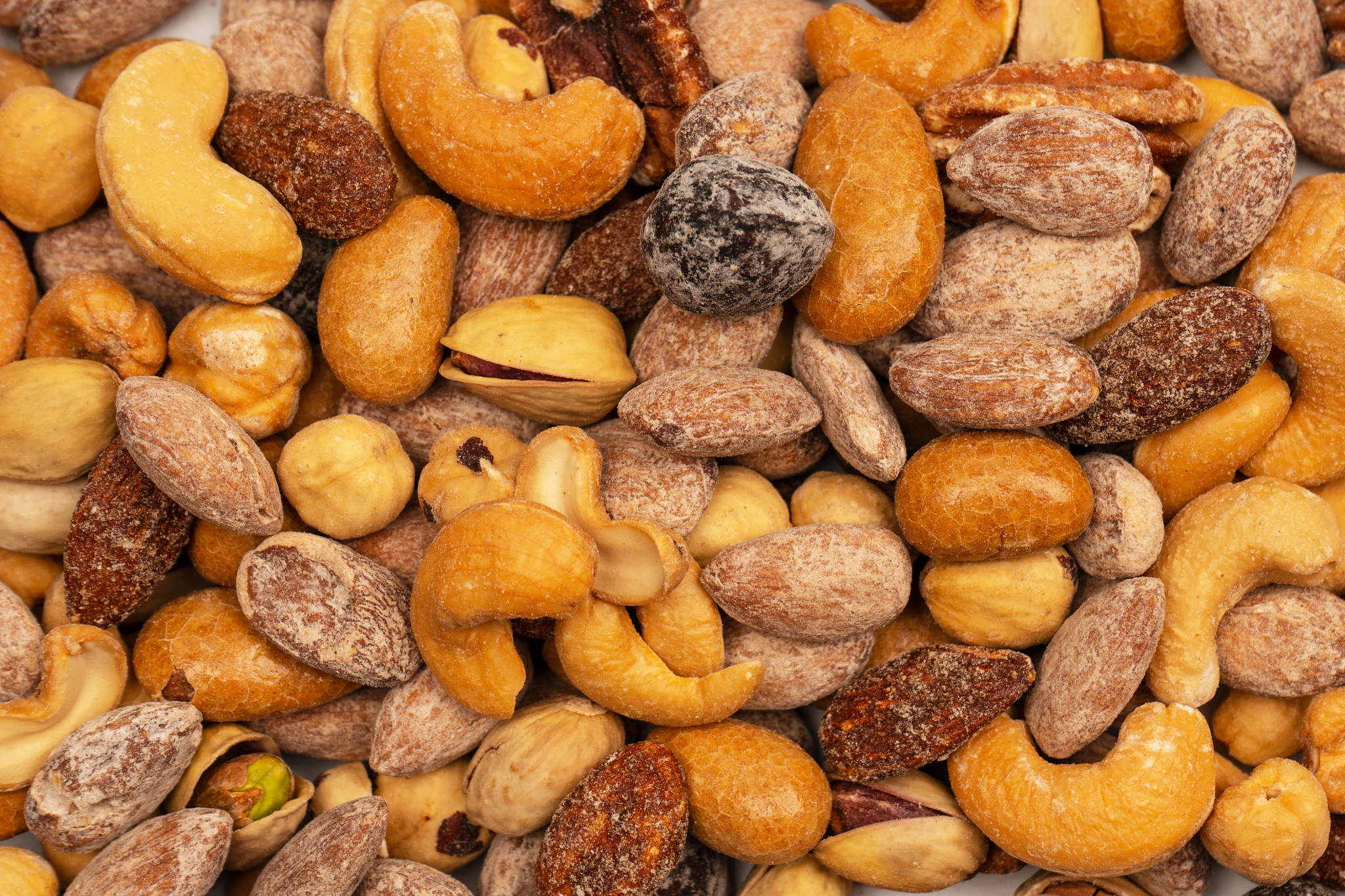 An overhead, close-up view of a variety of roasted and salted mixed nuts, including almonds, cashews, pistachios, and pecans.