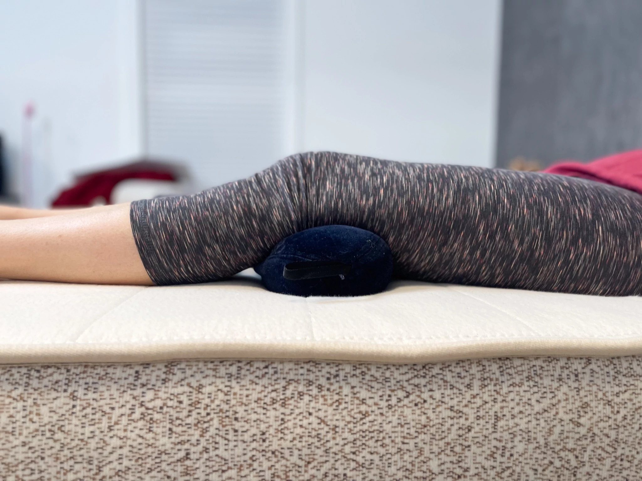 A person lying on their back on a mattress with the Tempur-Pedic All-Purpose Pillow under the back of their knees