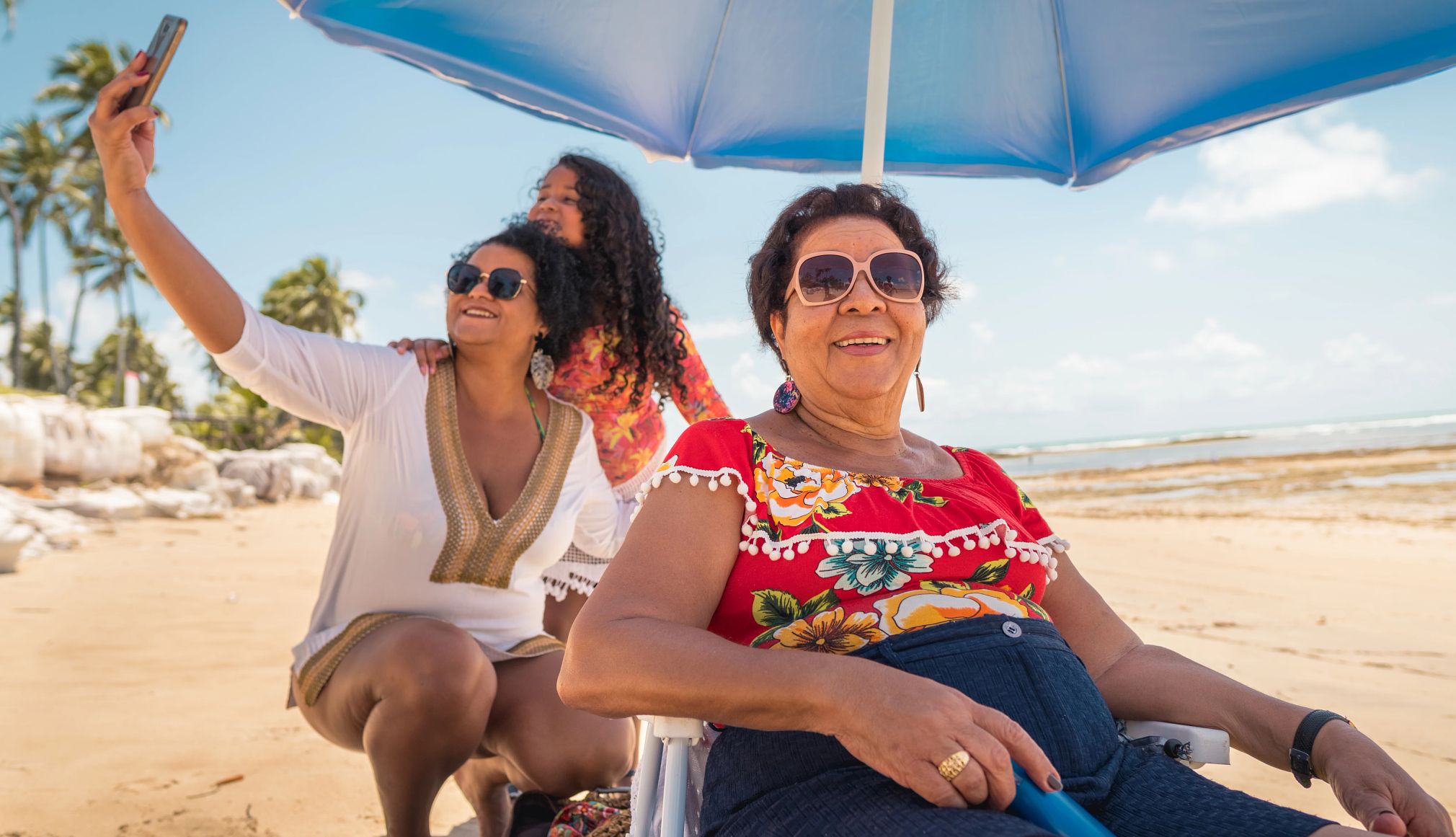 How to stay safe in summer heat, humidity three generations of woman taking a selfie underneath a beach umbrella