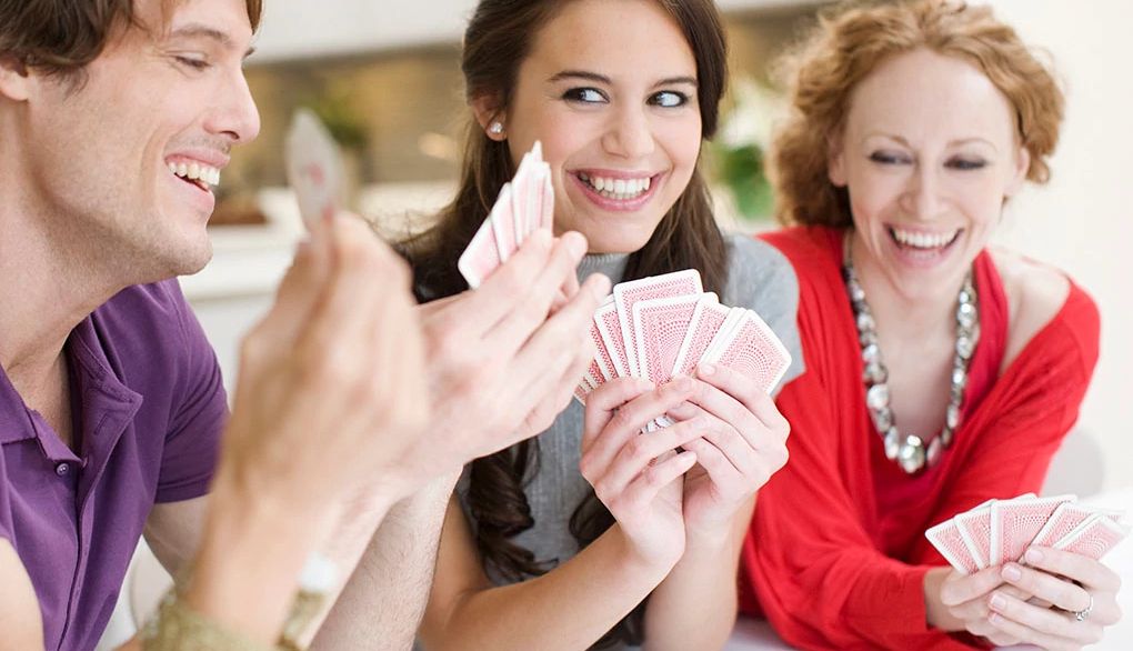 Play card games to enjoy time with friends A group of people smiling and playing cards together
