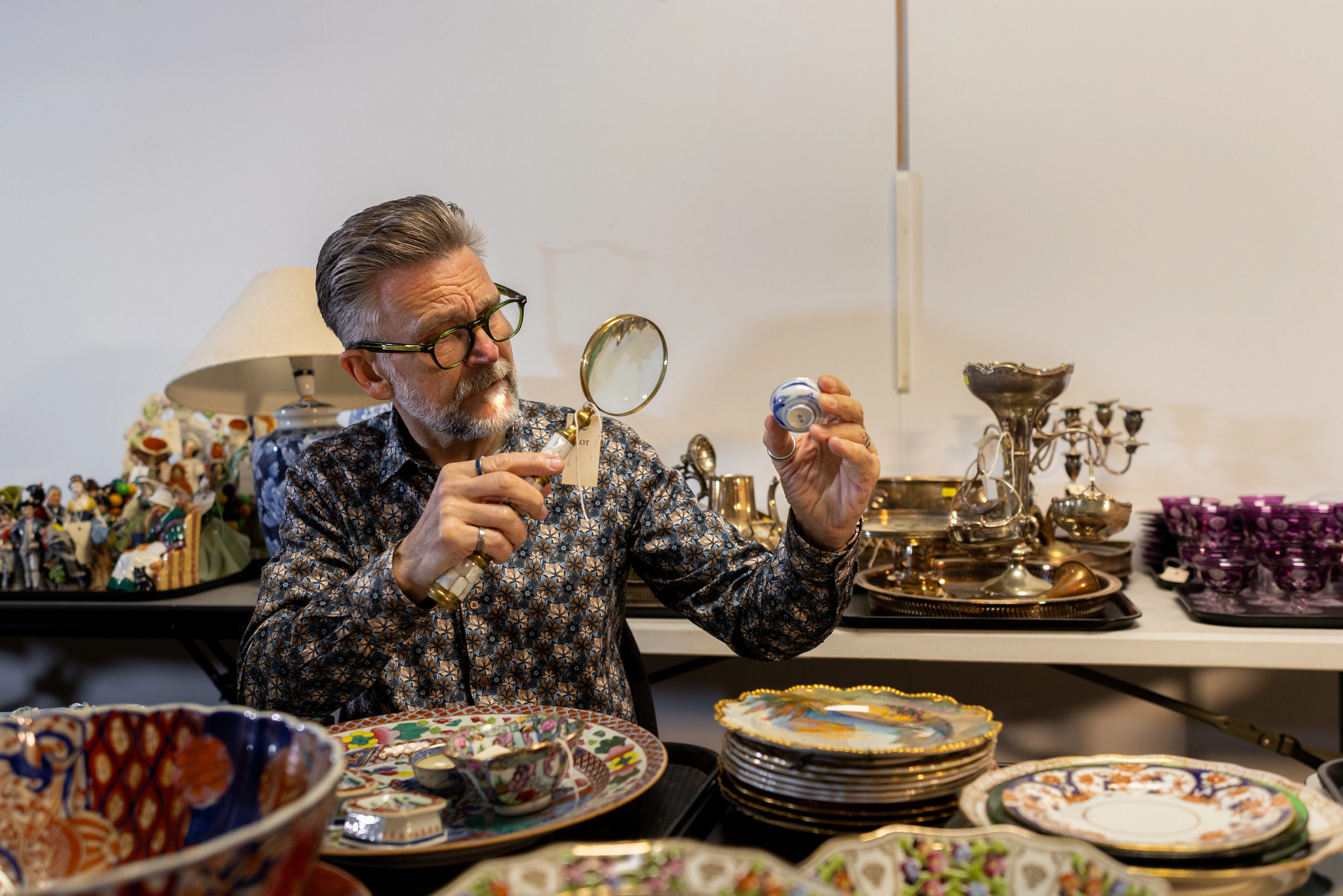 a photo shows a man examining an antique with a large magnifying glass