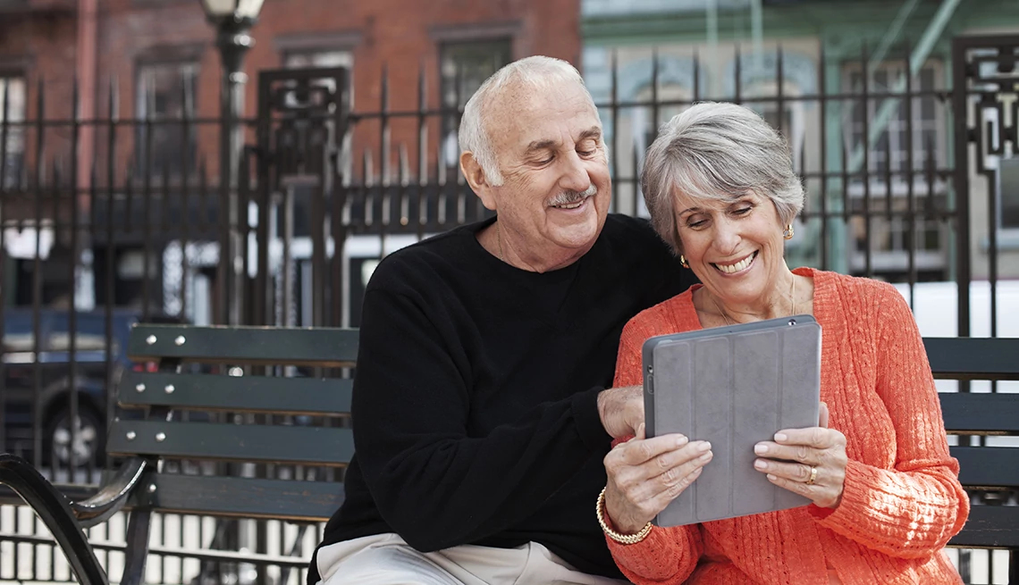 Una pareja de adultos mayores mira su iPad sentados en un banco en la calle Una pareja de adultos mayores mira su iPad sentados en un banco en la calle