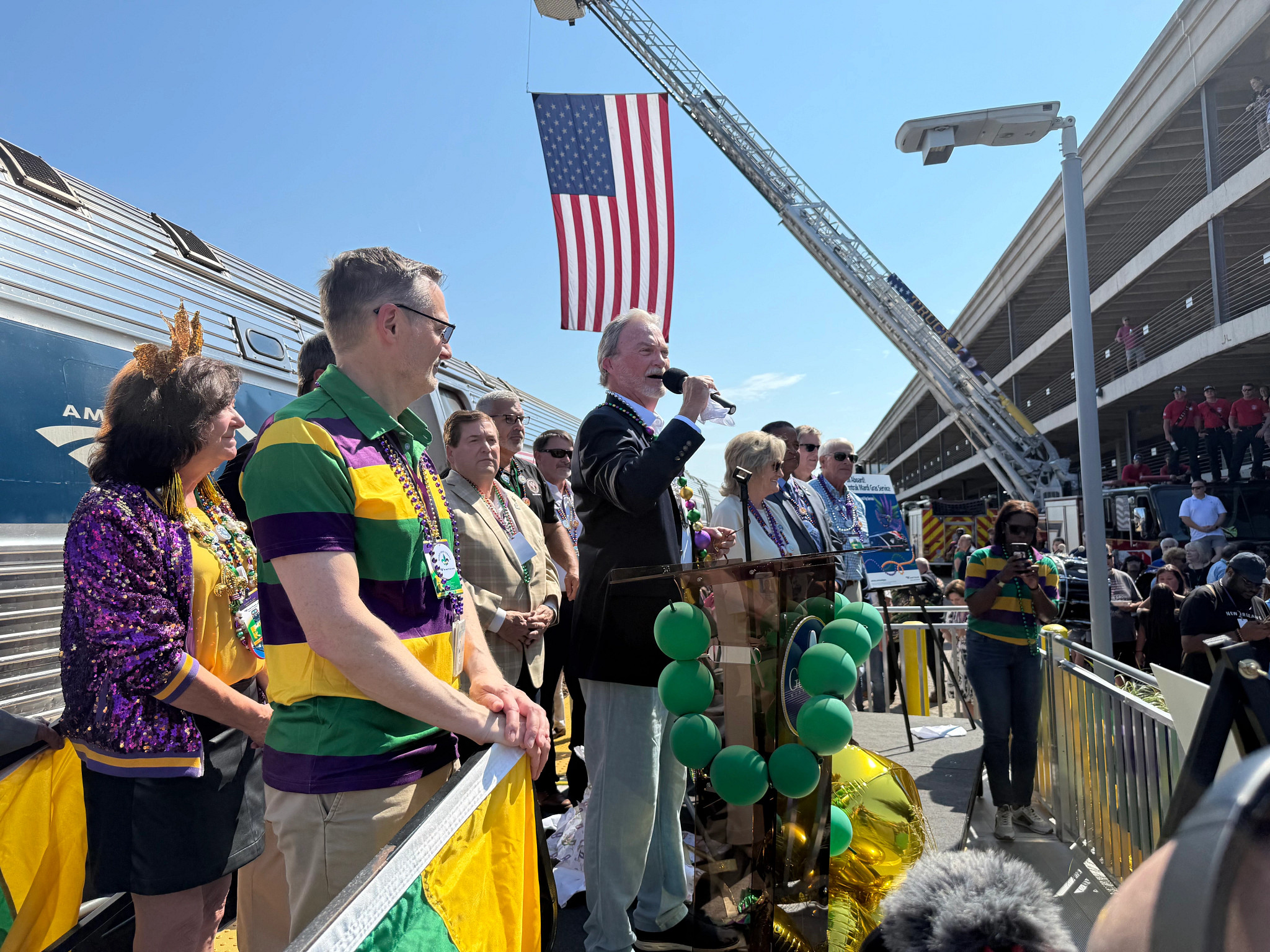 A man addresses attendees from a decorated podium outside of Amtrak train