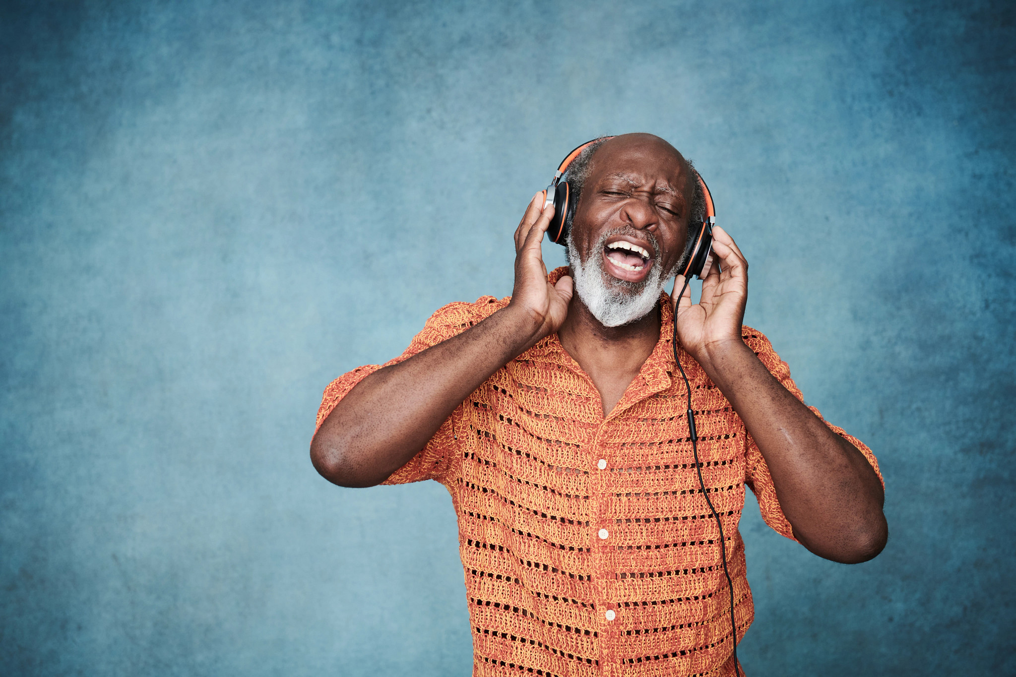 Close-up portrait of a mature man wearing headphones and singing to the music.