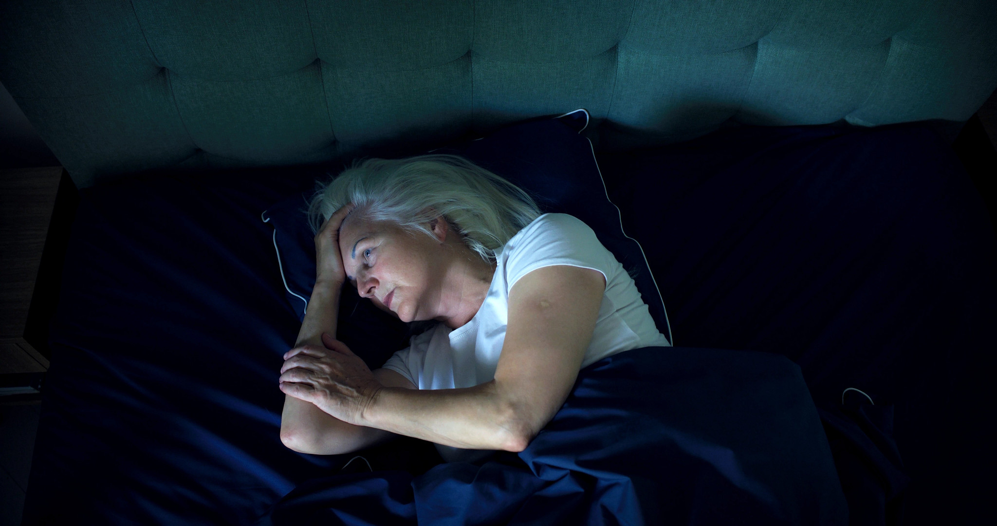 Older woman lying awake in bed at night, appearing tired and unable to sleep