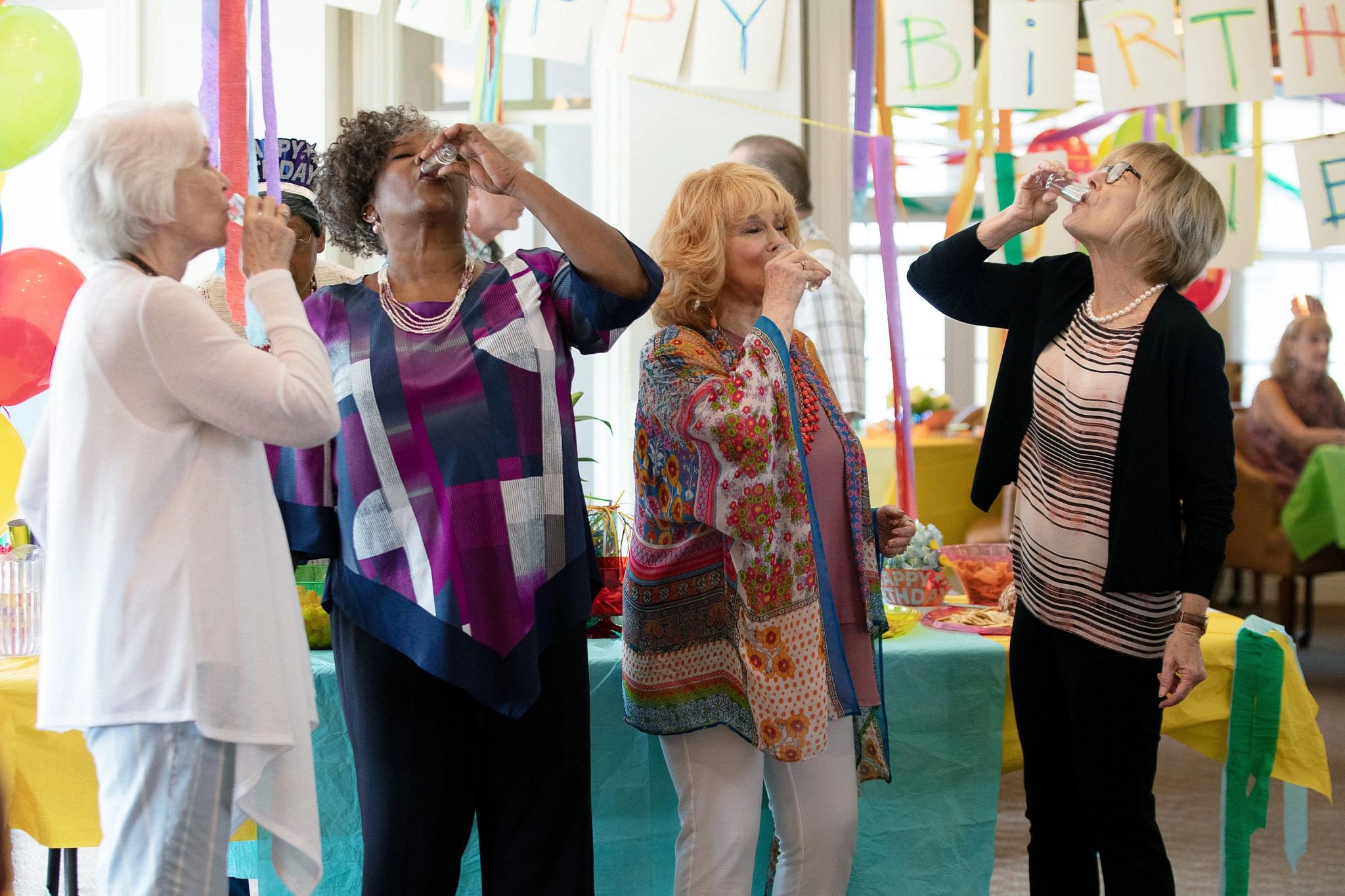 Ellen Burstyn, Loretta Devine, Ann-Margret and Jane Curtin raise small glasses during a birthday celebration decorated with colorful streamers and balloons