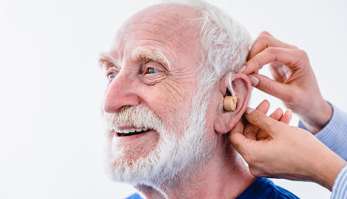 Hearing aids can slow cognitive decline and improve brain health A man getting hearing aids installed by another person on a white background