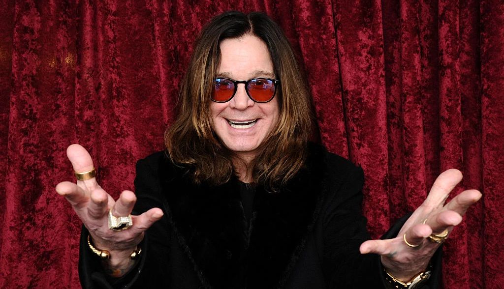 Ozzy Osbourne posing for a portrait with his hands facing up in front of him
