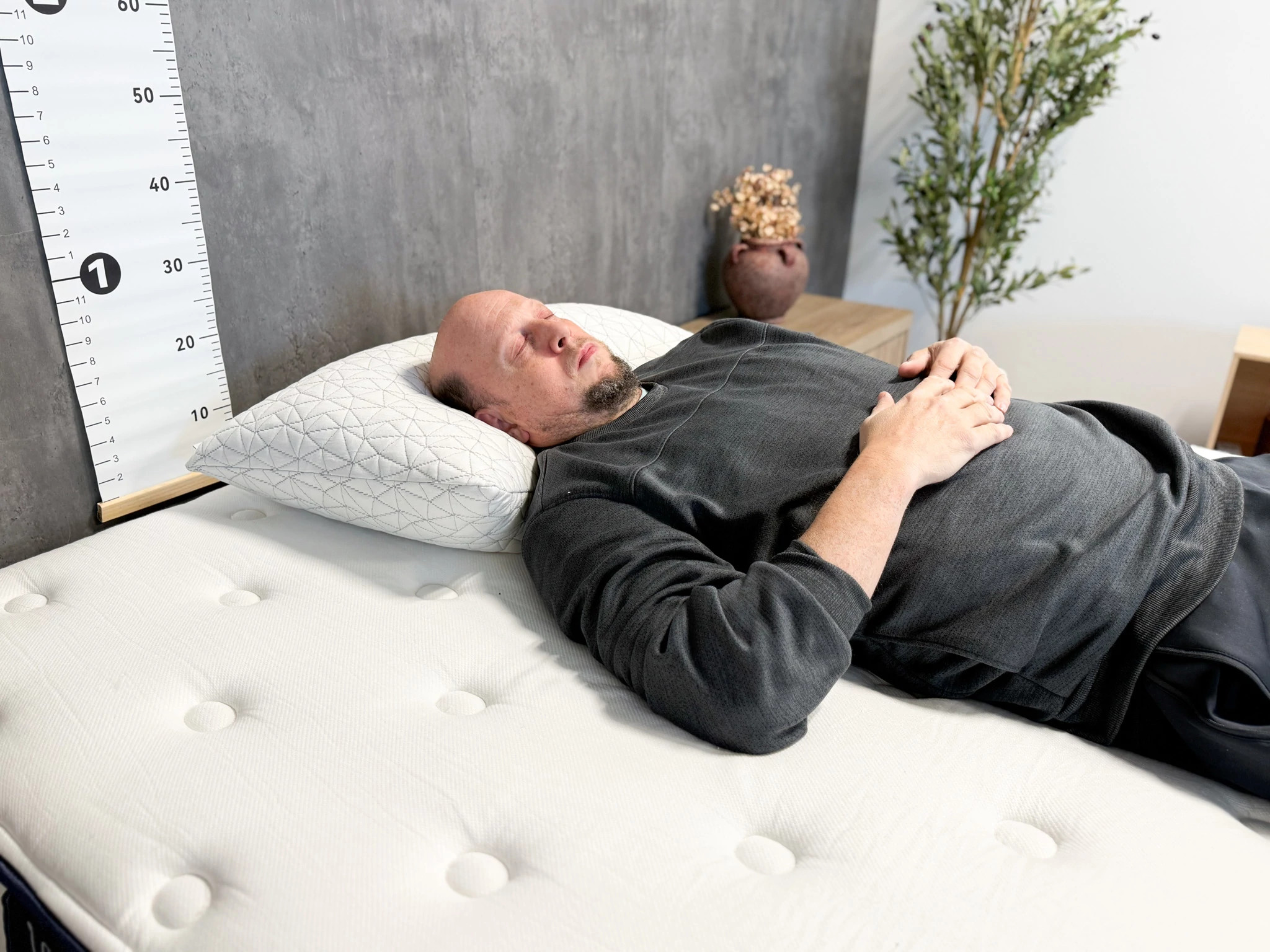 A man lying on his back on a mattress with his head resting on the Coop Original Adjustable Pillow