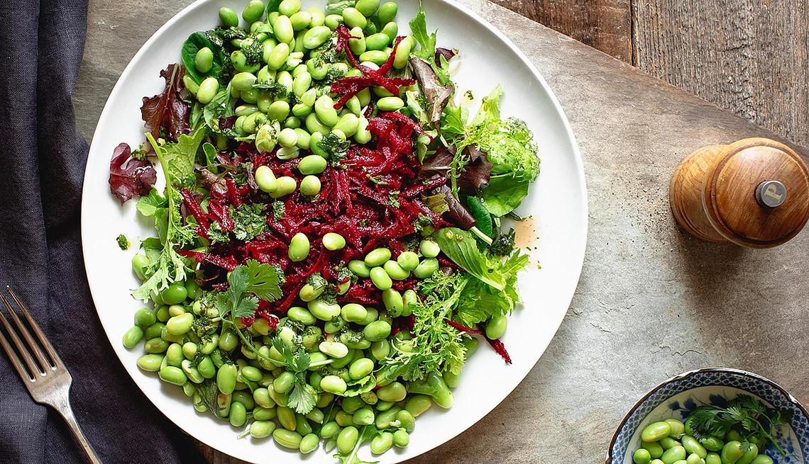 A close-up view of a green salad with edamame and beets on a plate