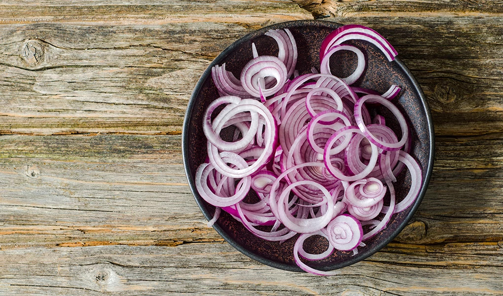 A bowl of sliced red onions on a wood background