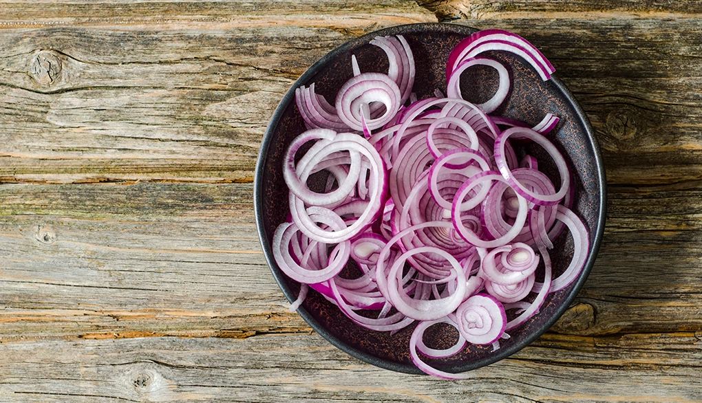 A bowl of sliced red onions on a wood background