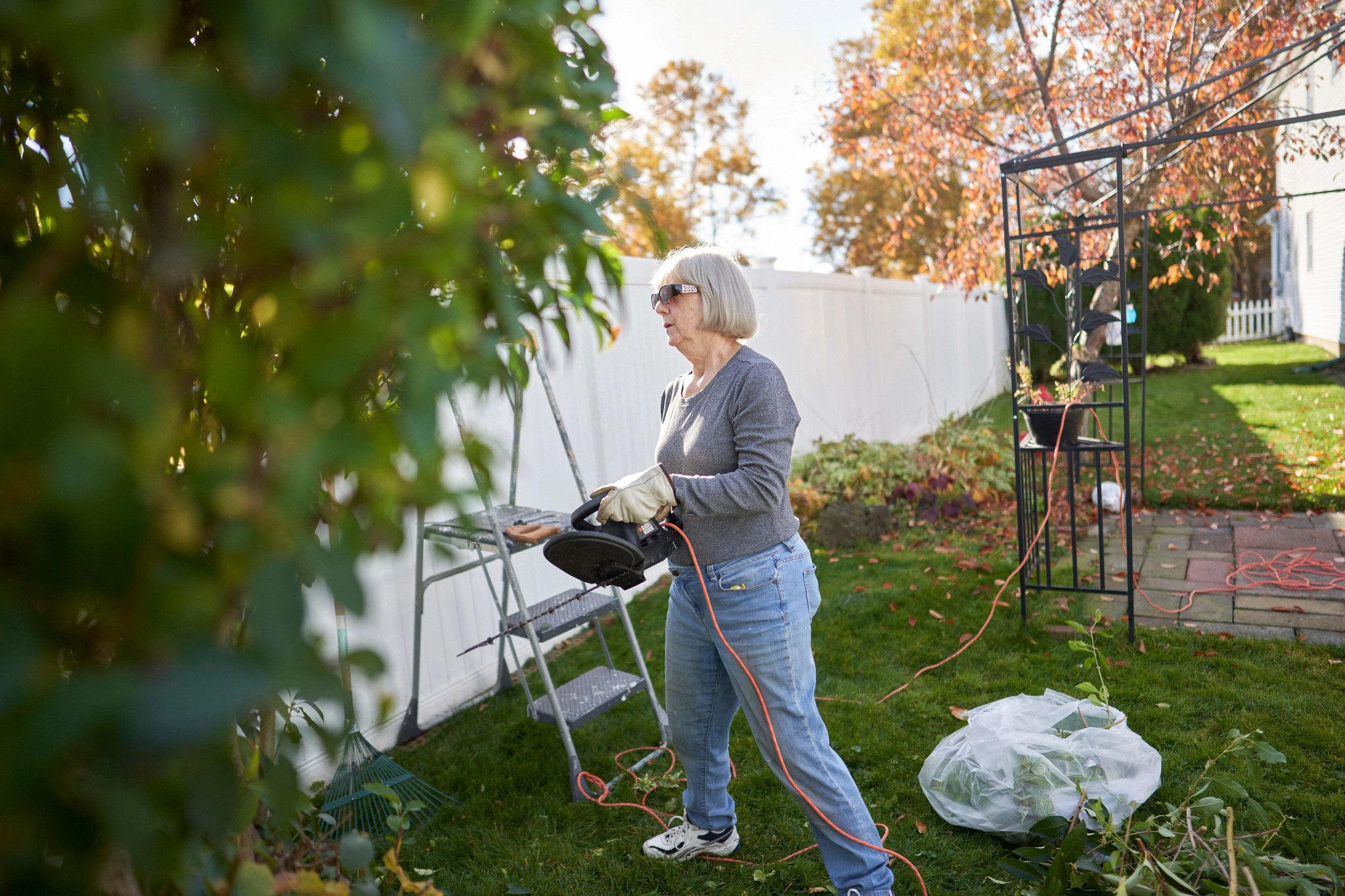 a photo shows an older adult woman in her garden working with a hedge trimmer