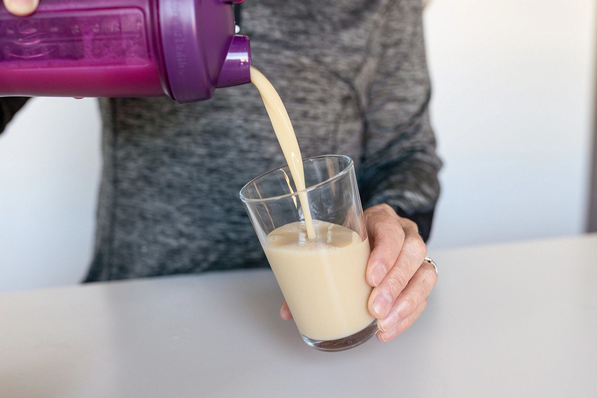 A person pours Sunwarrior Protein Warrior Blend drink from a purple shaker into a glass