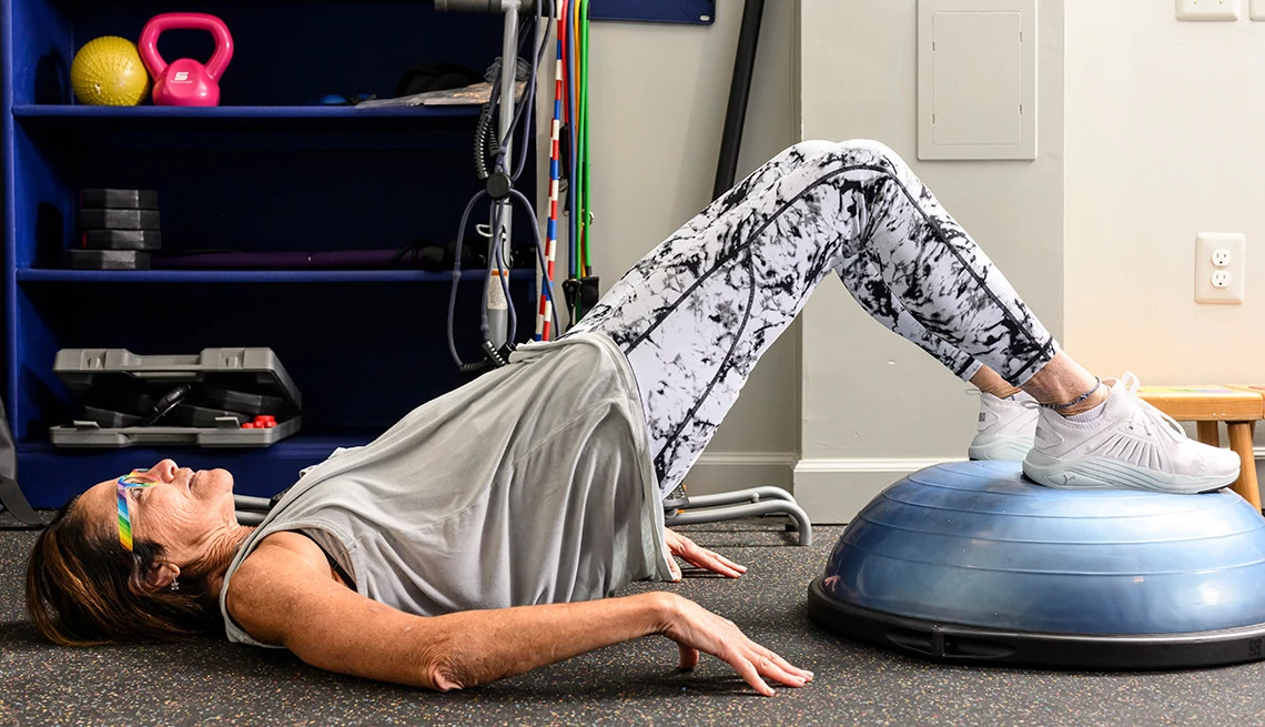 Person performing a hip bridge exercise with feet on a blue balance ball in a home gym