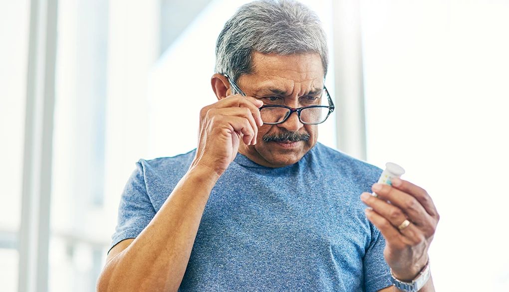 Huperzine A is a supplement that has been tested as a treatment for dementia and Alzheimer's A man wearing reading glasses to check the label on a bottle of supplements