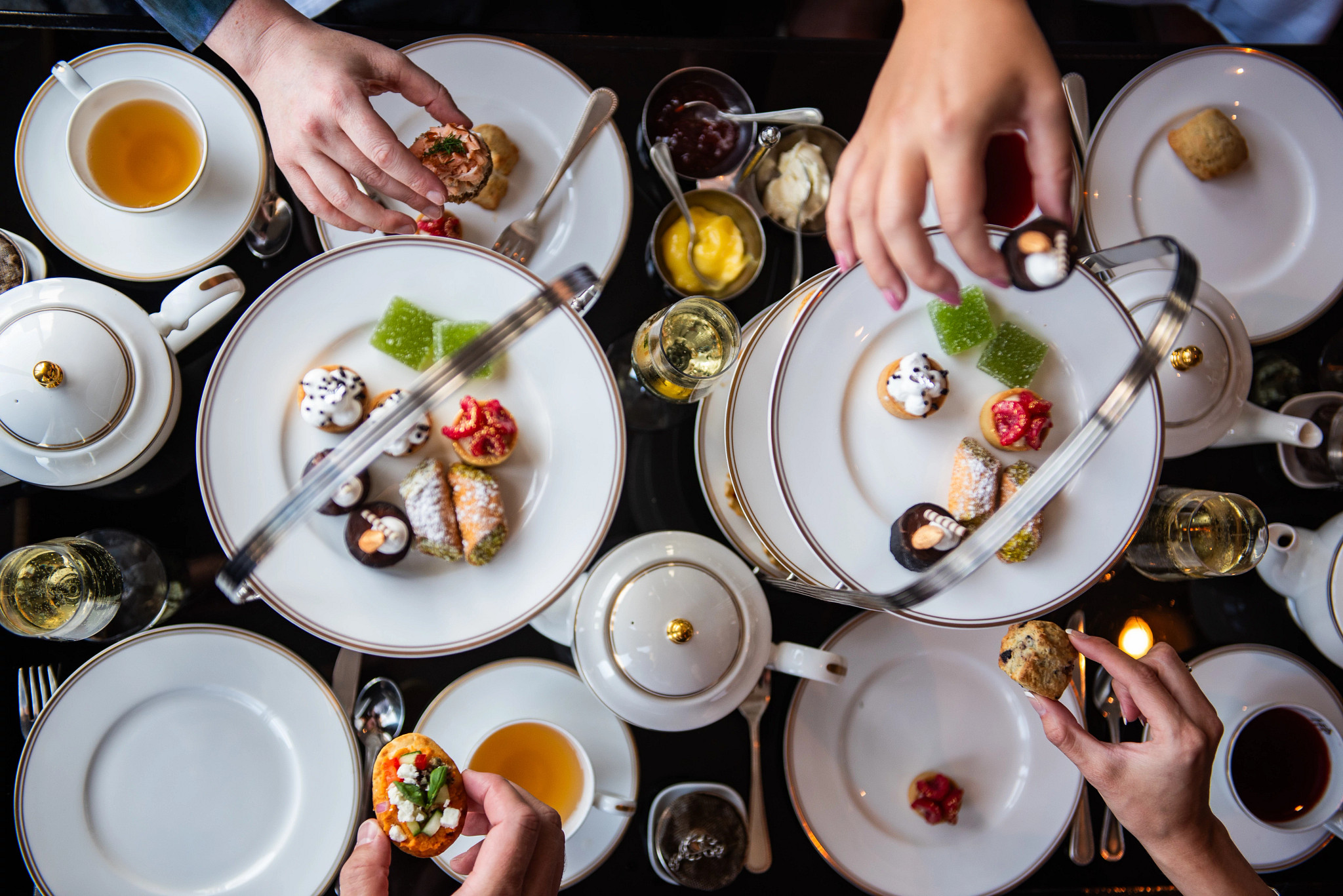 tea cups on a table where people are reaching for desserts 