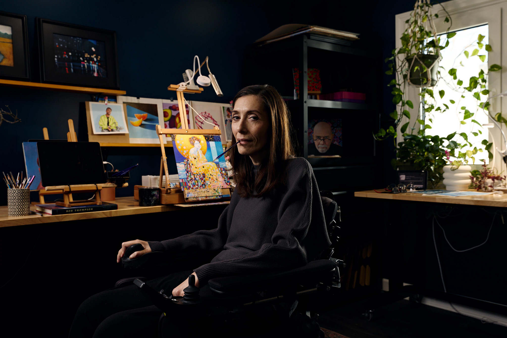 mariam pare holding a paintbrush in her mouth while posing for a portrait