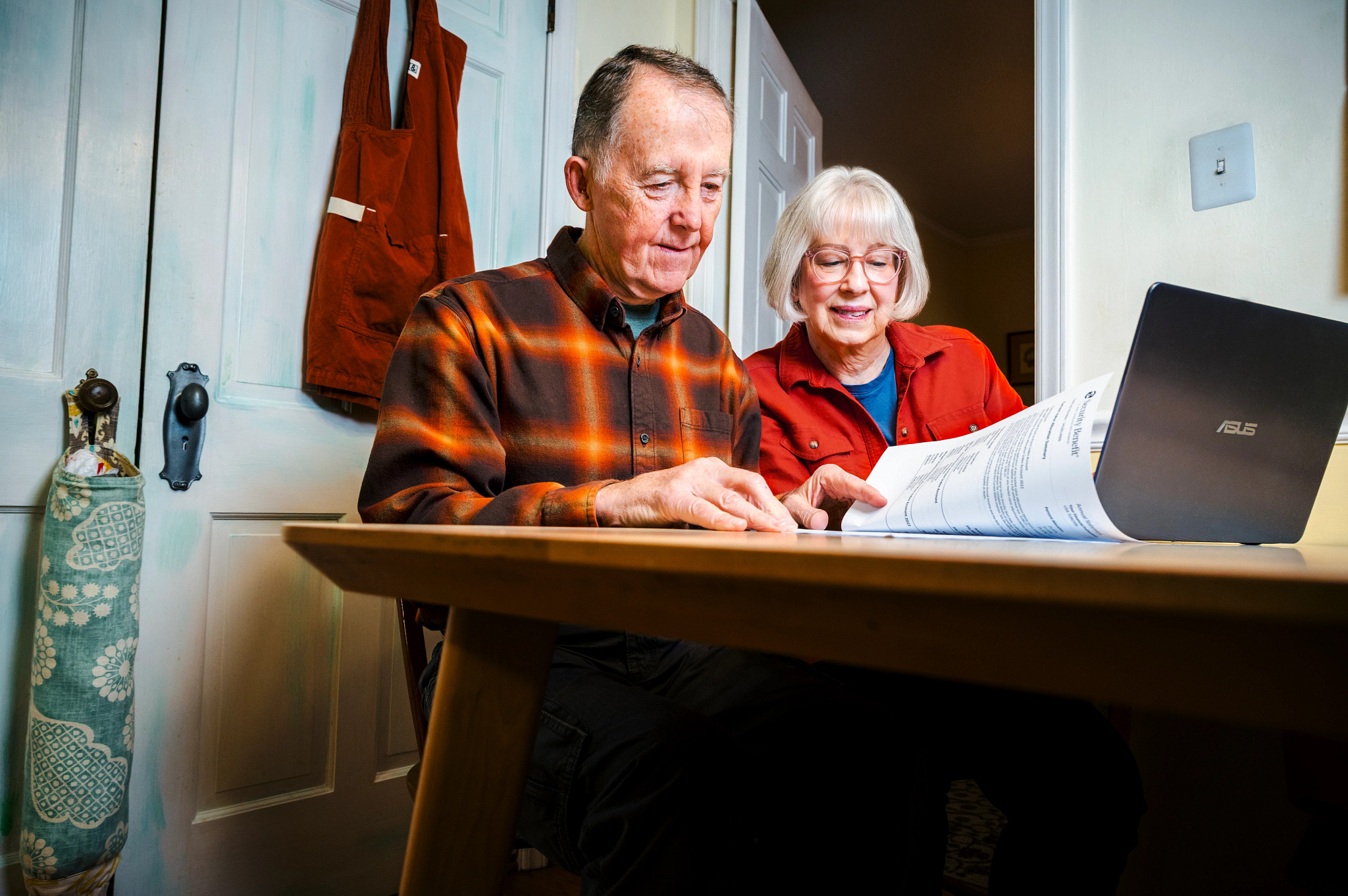 an older man and woman sit at a table, looking through annuity paperwork