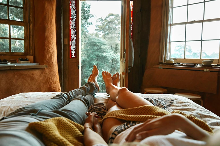 An image of a man and women's legs in bed, where they are lounging together and holding hands.