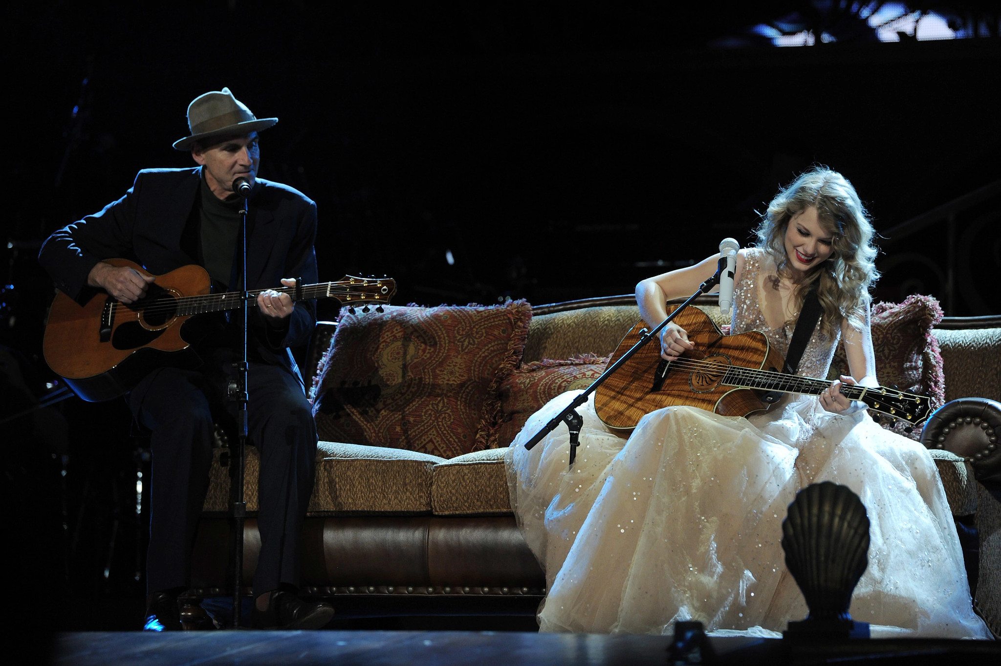 James Taylor and Taylor Swift sitting on couch playing guitar; microphone in front of each of them