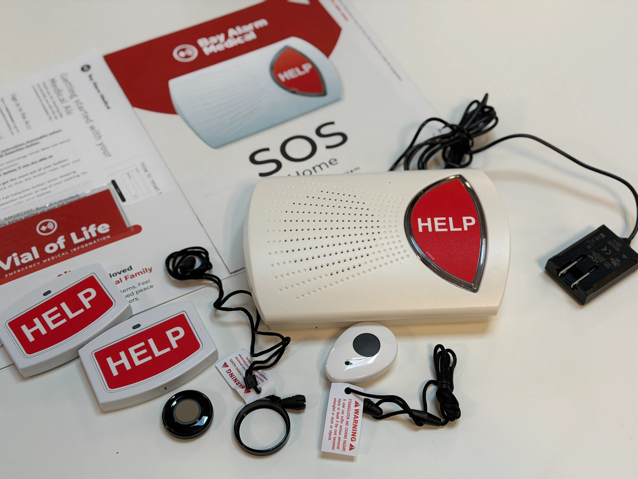 The Bay Alarm Medical SOS Home device next to the manual and accessories on a white table.