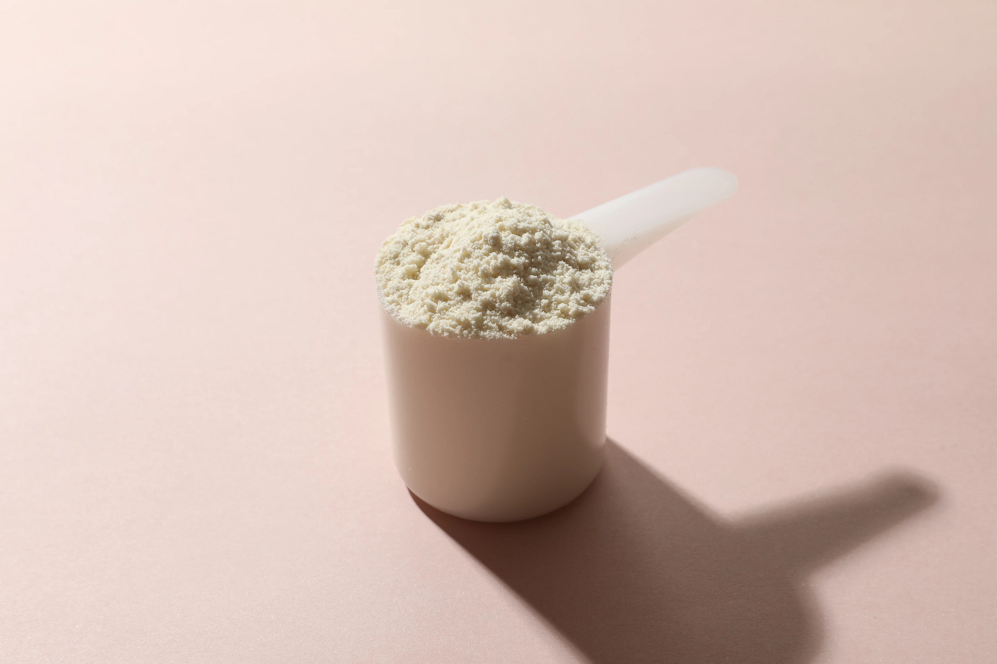 A scoop of protein powder on a pink background