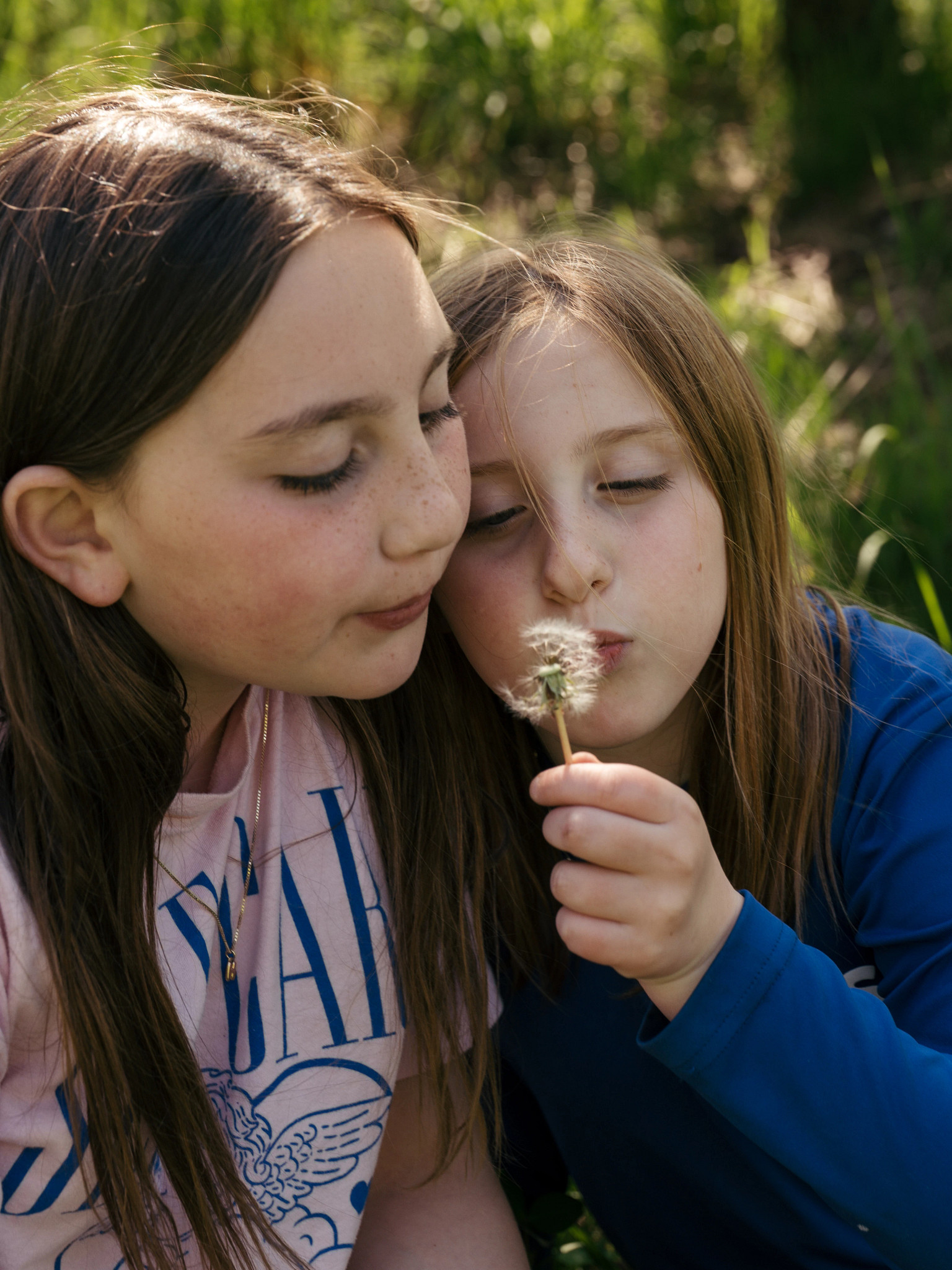 Helen and Lena Ginsberg outdoors blowing dandelion seeds together in a natural setting