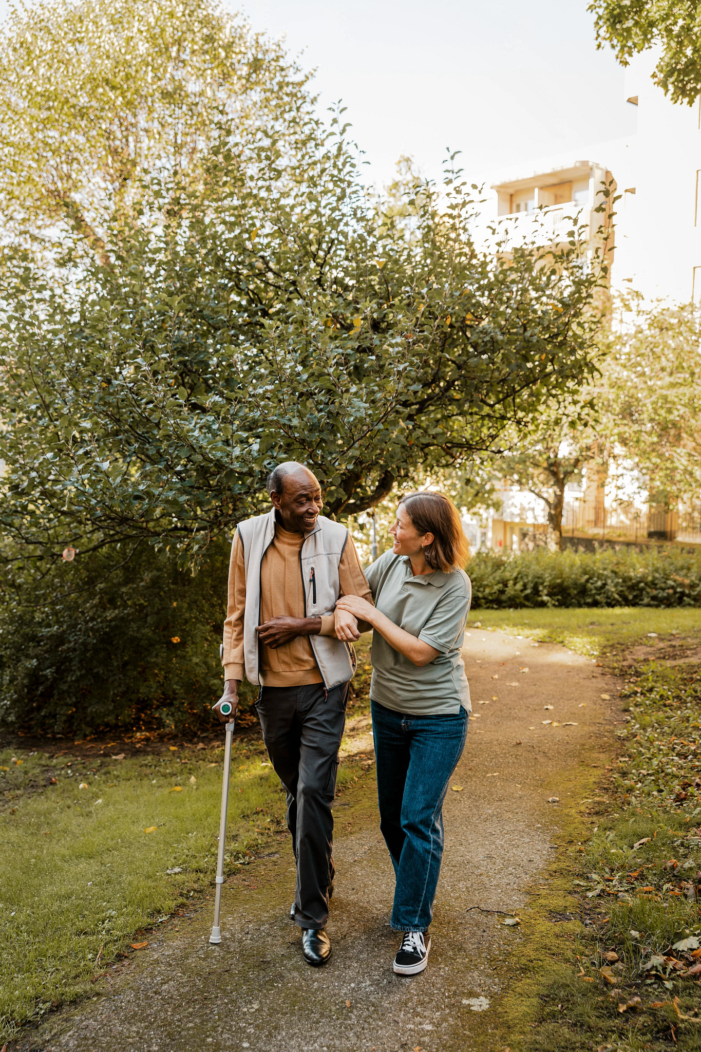 Female nurse and senior male walking with arm in arm on footpath at park