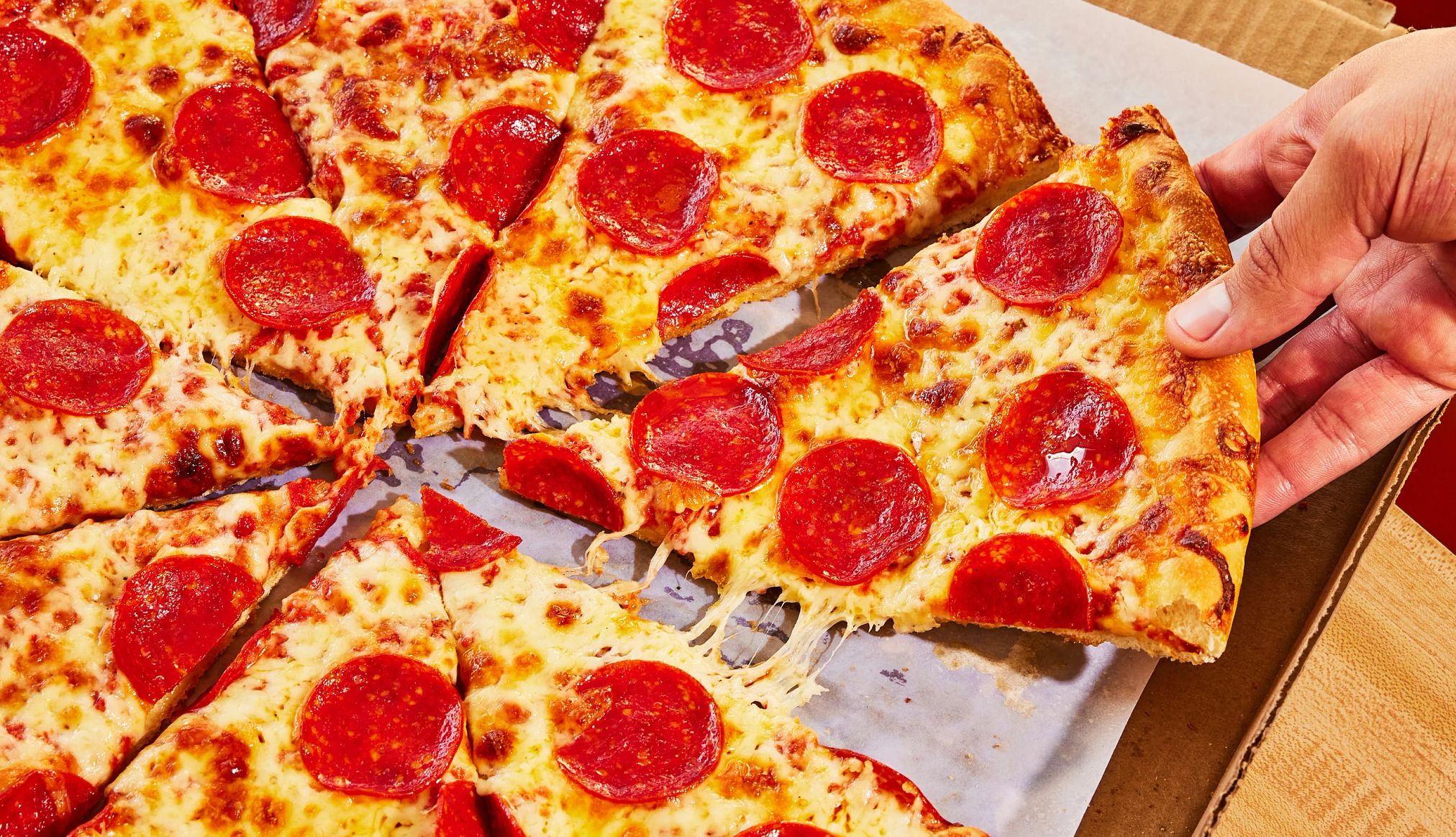 National pizza day deals a hand pulling a slice of pepperoni pizza from a box