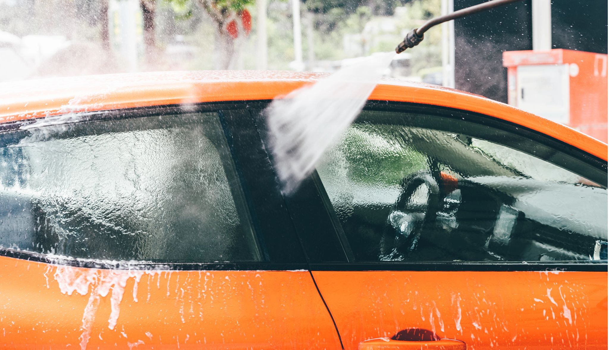 Cleaning the exterior of vehicle Car wash hose washing outside of orange vehicle