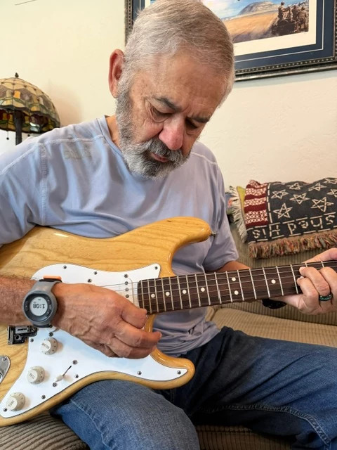 man wearing a smart tremor wristband plays a natural wood electric guitar
