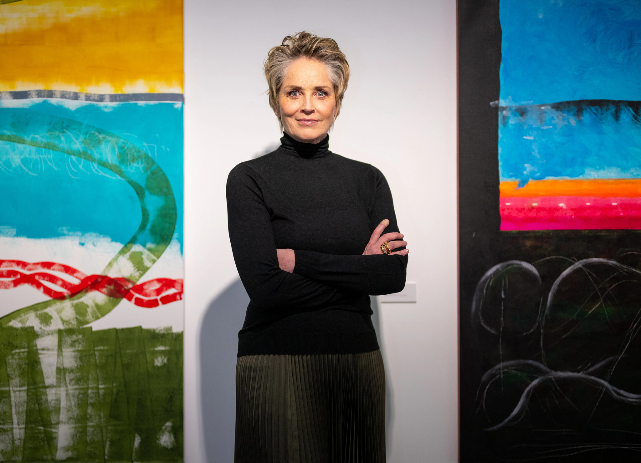 sharon stone standing with arms crossed in front of artwork