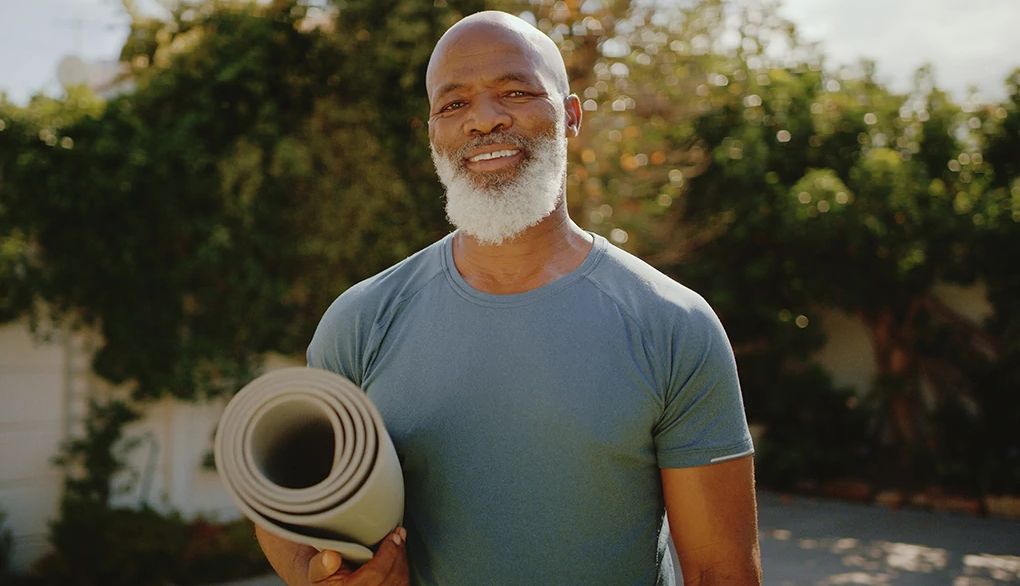 Yoga poses and breathing may help you calm your mind and strengthen your body A smiling man holding a yoga mat under his arm outside