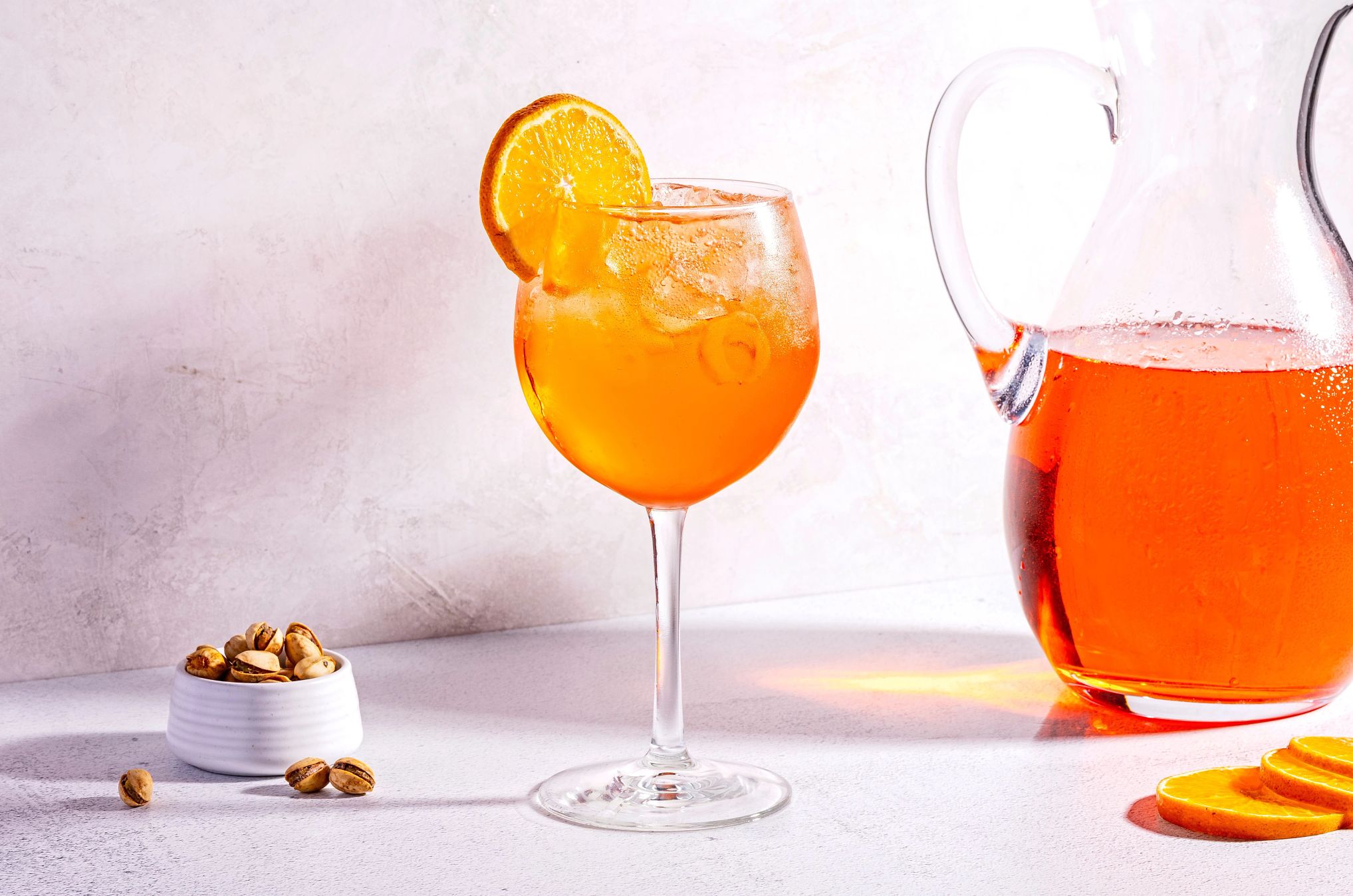 Aperol Spritz is often garnished with an orange a pitcher and a glass of Aperol Spritz on a table