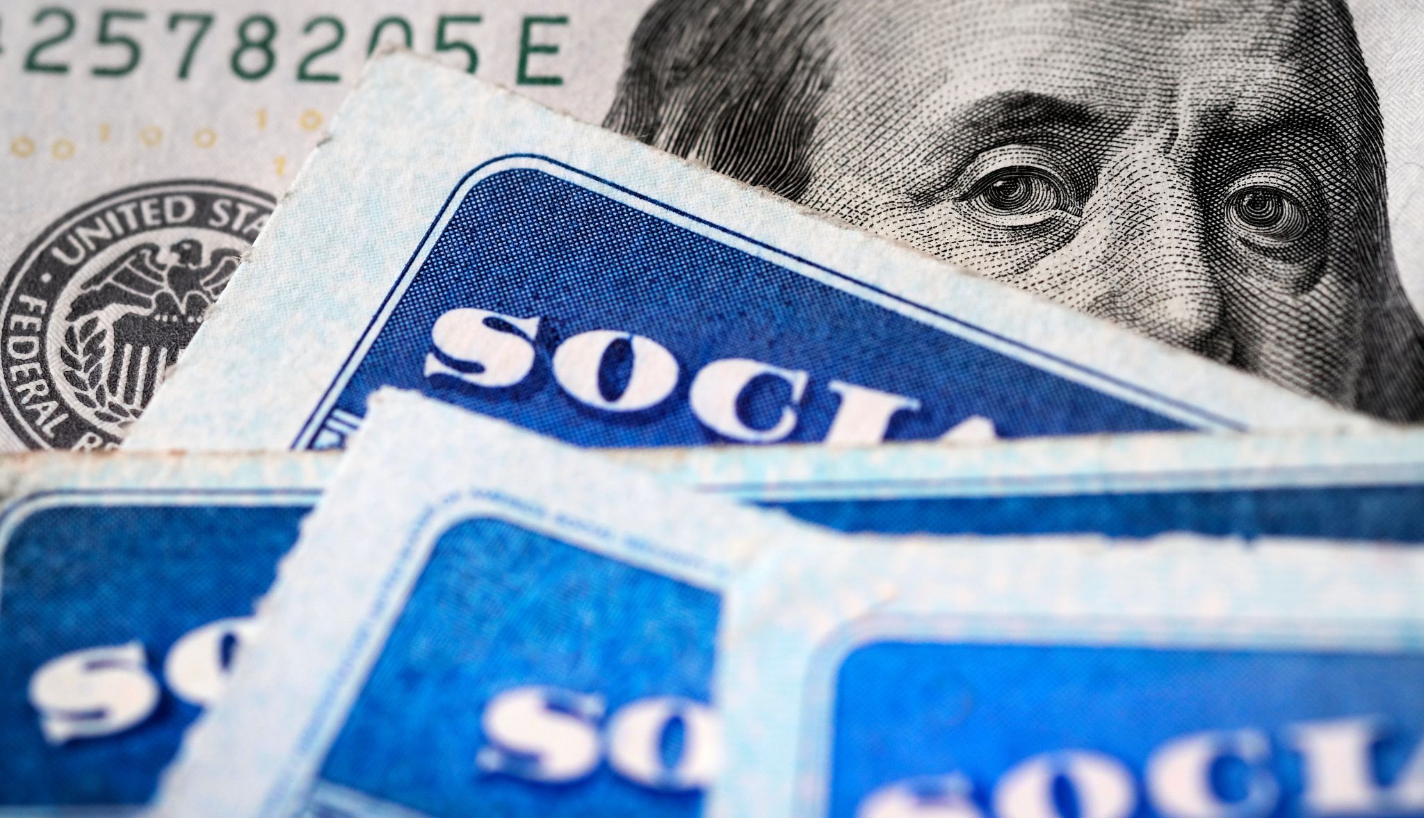 Several Social Security cards sit on top of a one-hundred-dollar bill. Several Social Security cards sit on top of a one-hundred-dollar bill.