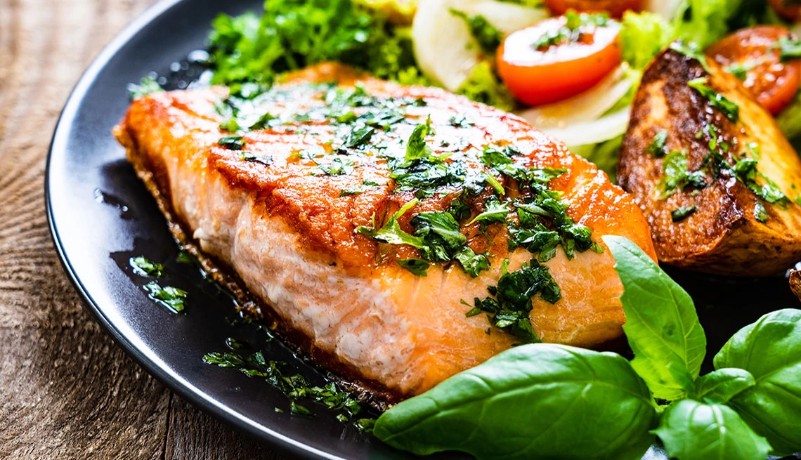 AARP® Personalized Nutrition cooked salmon with potatoes and salad on black plate sitting on a wood table