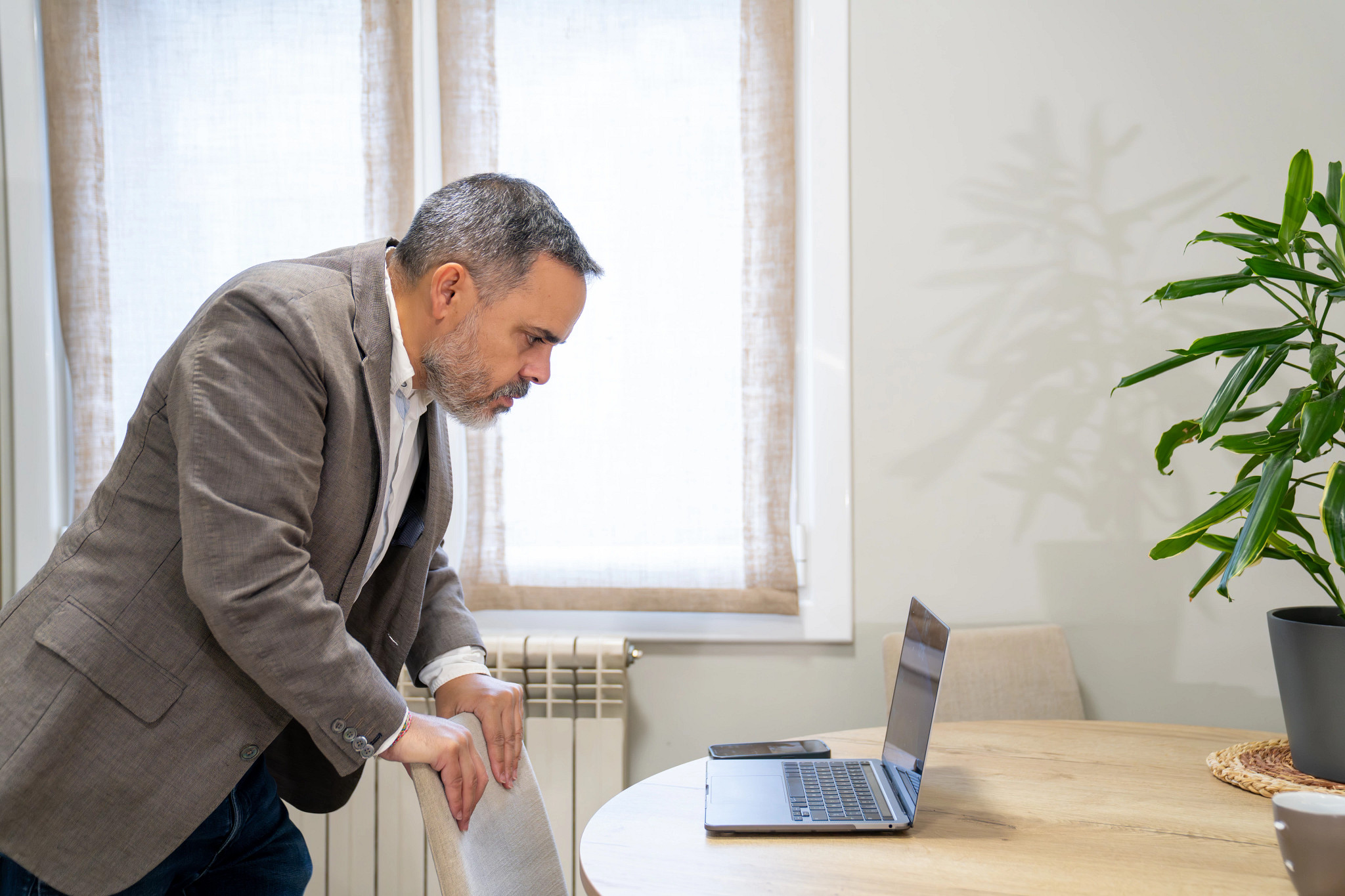 a photo shows an older adult man looking at a laptop on a kitchen table